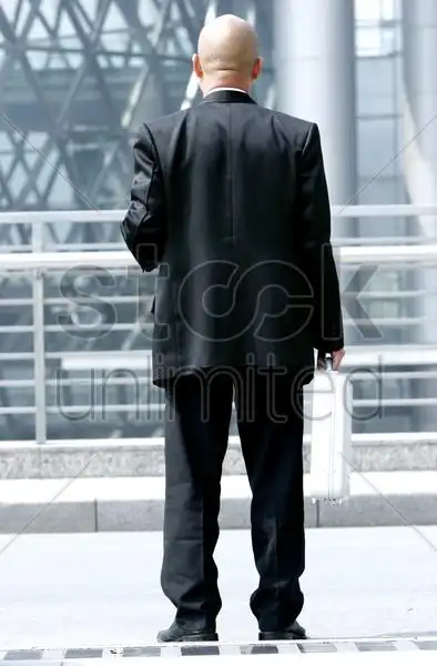 穿着西装,提着一个手提箱的光头男背影