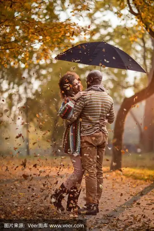 一对深情的非裔美国情侣站在公园的伞下.