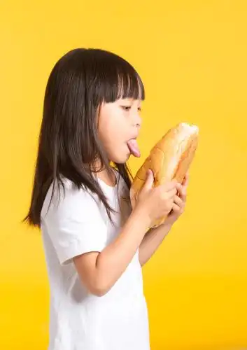 可爱的亚洲小女孩伸着舌头吃面包