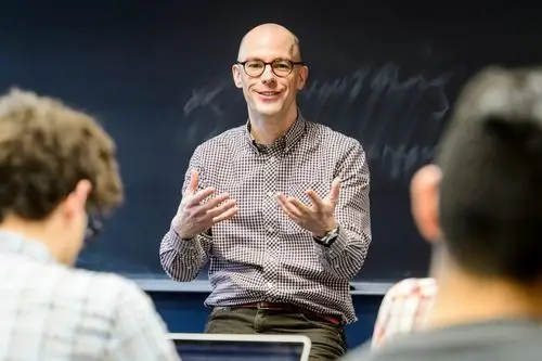 a male instructor wearing glasses and a collared shirt faces the