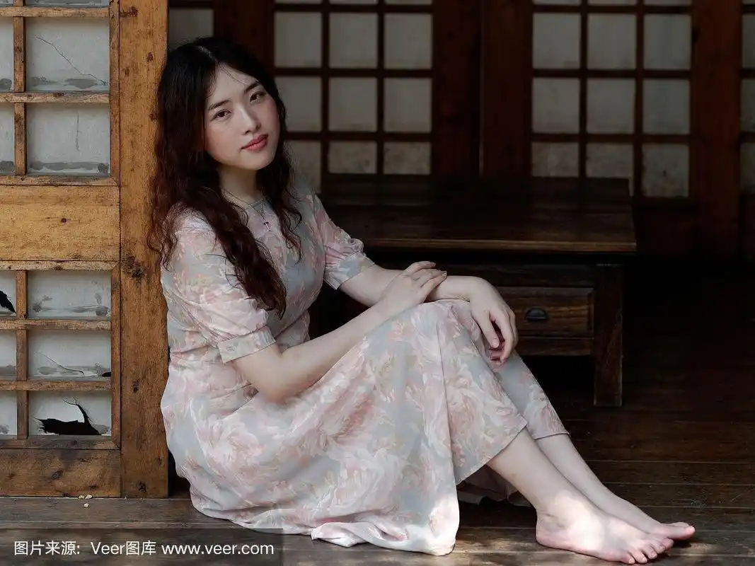 在木纸门上,带着孤独的表情看着镜头微笑,中国美丽的女孩在夏天的肖像