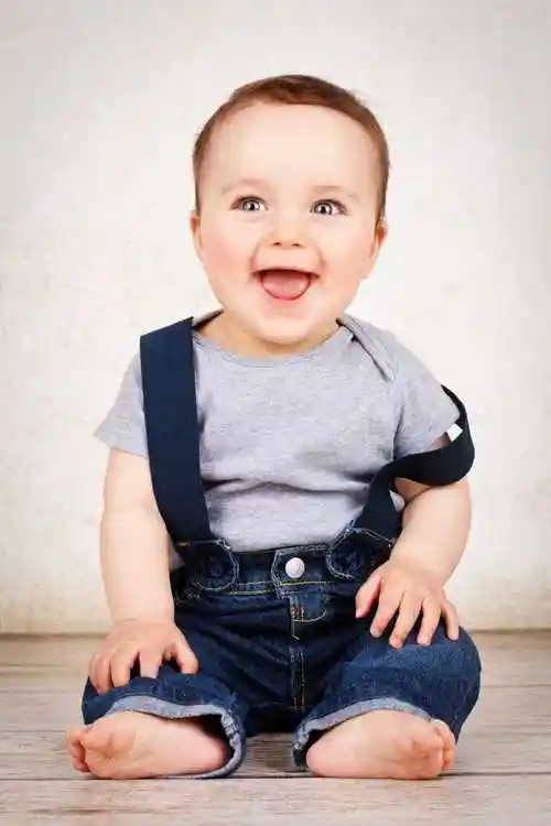 白色背景下坐在地板上的笑起来的小男孩