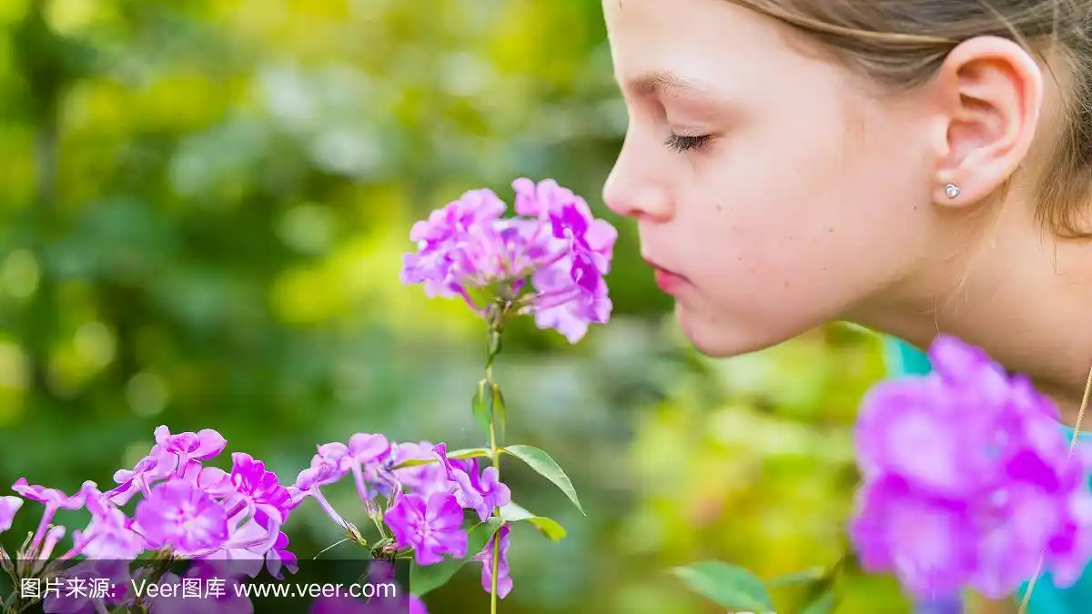 年轻漂亮的女孩闻着花园里的紫花