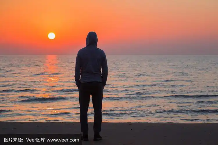 年轻的成年人站在沙滩上,凝视着海浪和橙色的夕阳.夏夜宁静的气氛.