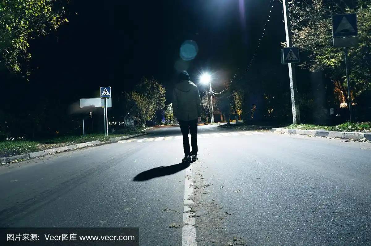 一个神秘的人孤独地站在街上,在空荡的城市的汽车之间,走在夜晚的街道