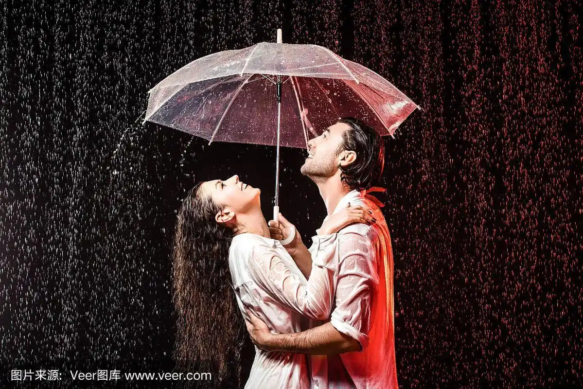在黑色背景下,一对情侣穿着白衬衫打着伞站在雨中