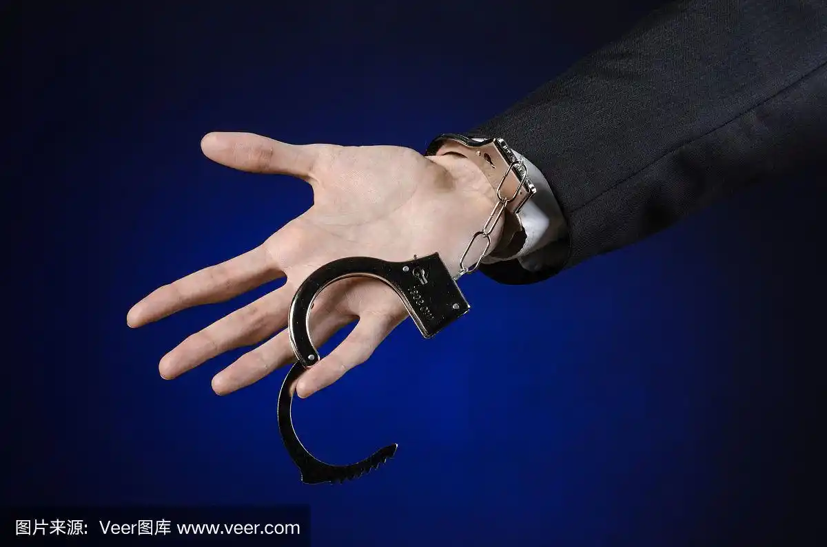 腐败与贿赂主题:商人身穿黑色西装,双手戴着手铐,以深蓝色为背景,在