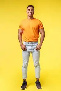 垂直的全身摄影棚拍摄年轻的时髦男人,面具般的身体,站着的橙色t恤和