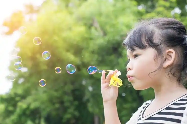 绿色树木前一个亚洲小女孩再吹泡泡