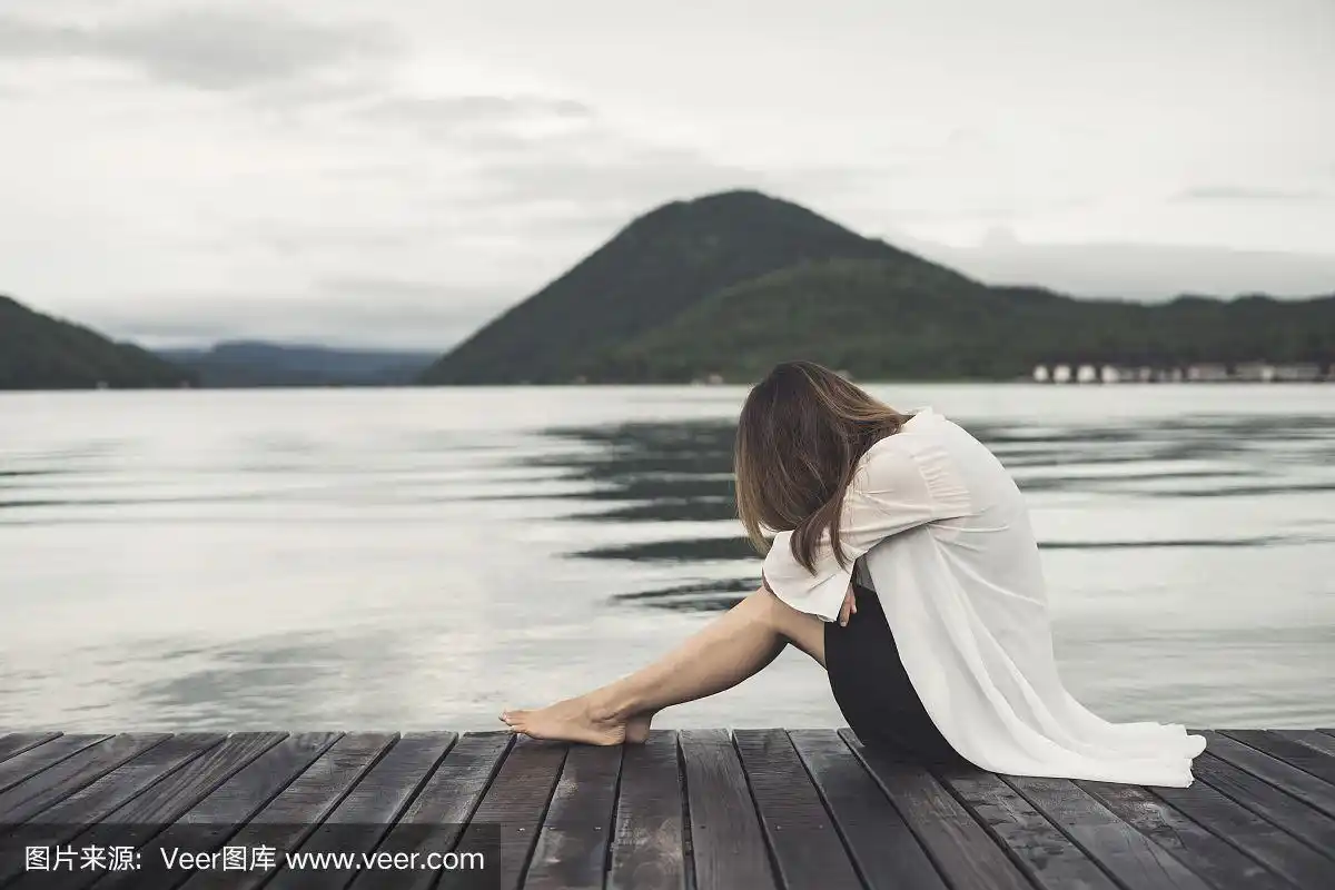 孤独的女人坐在木码头上望着湖面