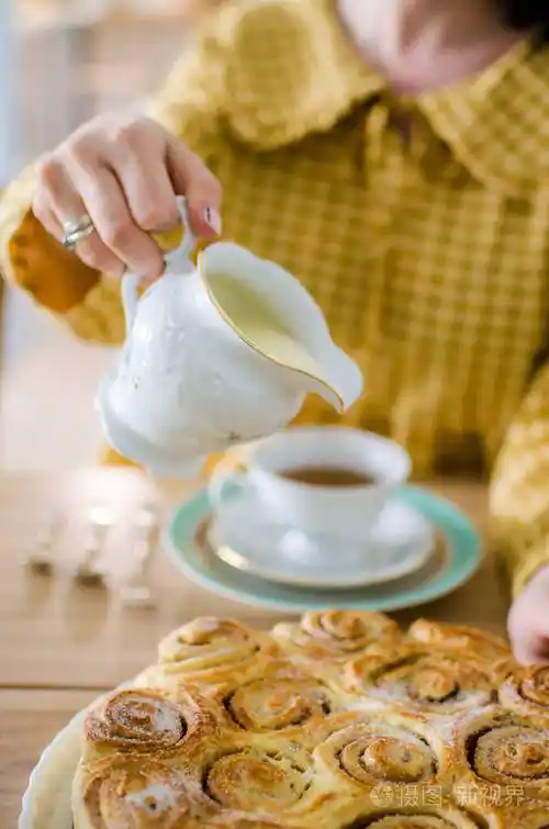 一个女人把牛奶倒进杯子里桌上放着芳香的茶synabons在桌子上茶点时间