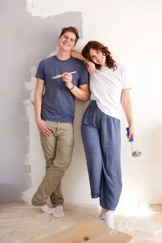 用油漆刷子站在墙边的幸福情侣的全身肖像