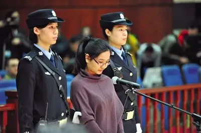 被告人卢梅低着头,站在朝阳法院刑事审判庭的被告席上.