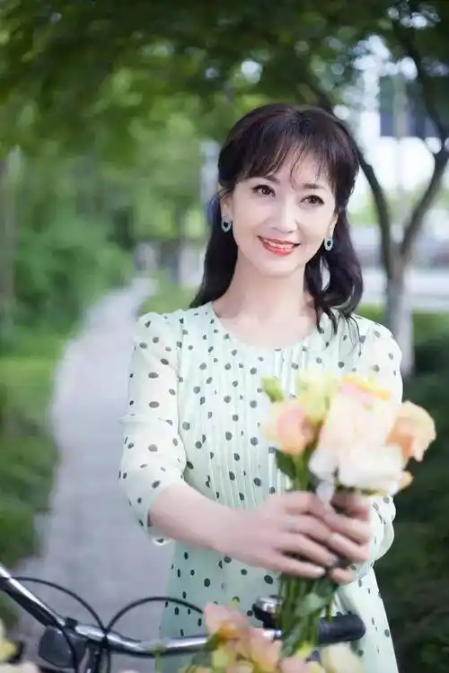 看这张照片里面的赵雅芝,穿着一件绿色的波点裙,手捧着一束花,看起来