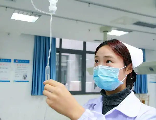 县总医院青年护士细心检查病人的输液情况,调整输液滴数.