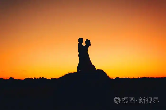 对夫妇抱着橘黄色的夕阳为背景