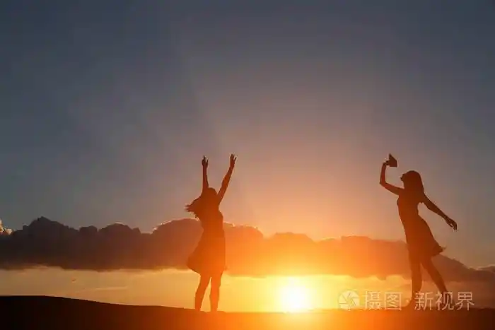 两个女孩在美丽的日落和大海的背景下跳舞剪影