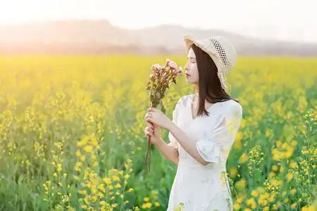 阳光下的油菜花海中少女手捧鲜花闻花香摄影图配图