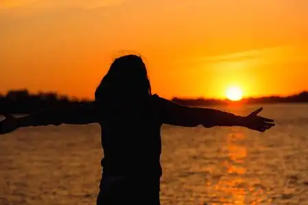 一个女孩的剪影在黄昏太阳红色日落手朝向太阳的背景下照片