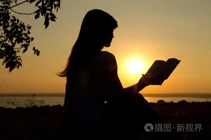 一个女孩在日落时阅读的剪影