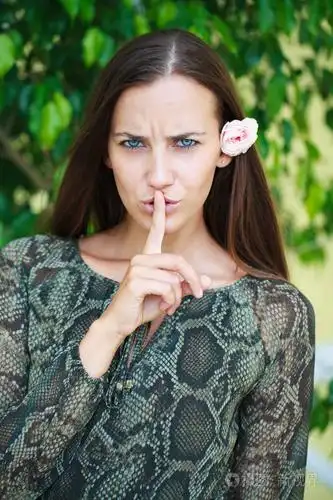 年轻美丽的黑发女人已经把食指放在嘴唇上作为标志的沉默,对绿色的