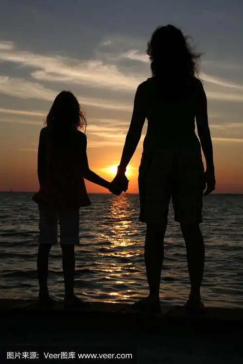 剪影母亲和女儿牵手在日落