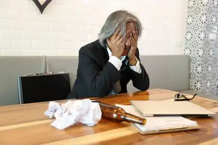 一位资深商人因生意失败而感到压力,电脑,手机,文件和木桌上的酒瓶