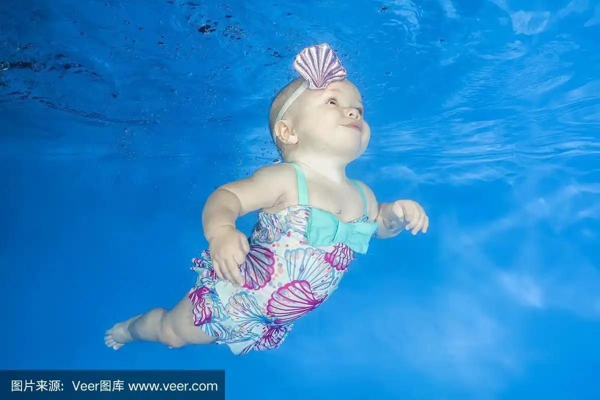 小女孩在学水下游泳.婴儿在游泳池里游泳在一个蓝色的水背景.