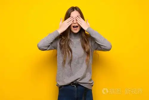 年轻的女人在黄色的墙上用手遮住眼睛惊讶地看到前方的情况