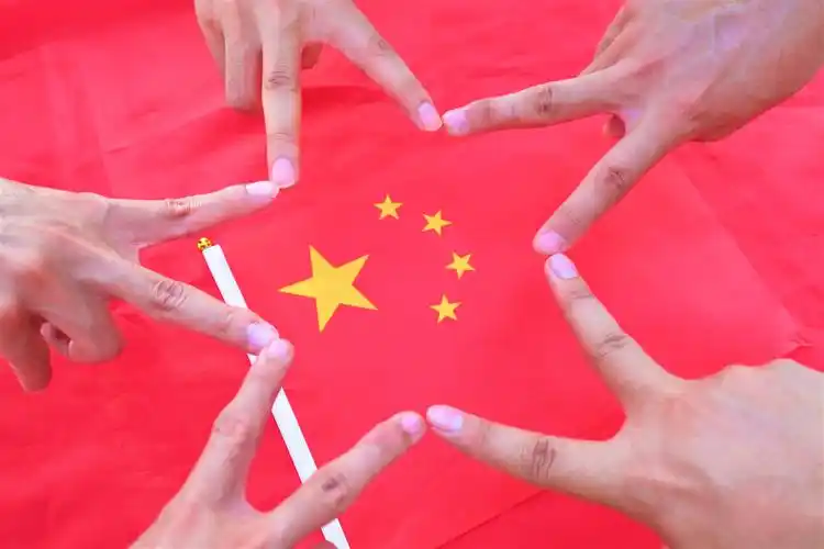 青年员工摆出五角星手型和手帖五角星形式与国旗合影,表达对祖国的