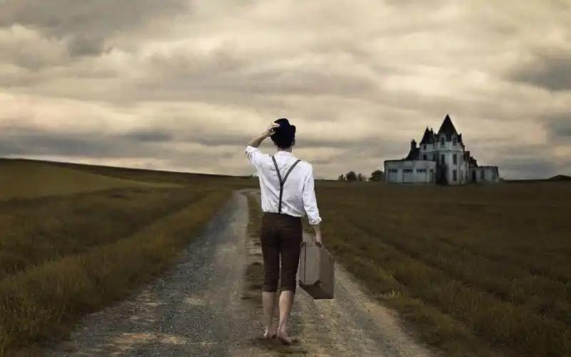 求这张穿白色衬衫的男生手提背包望向远方房子的背影图片!