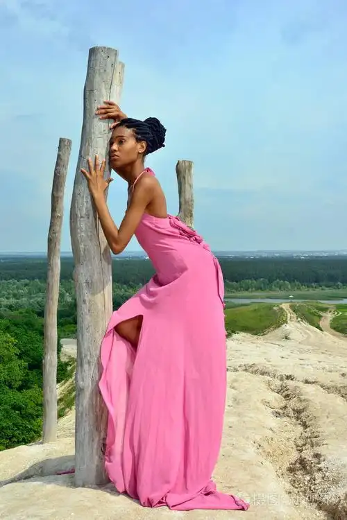 性感的非洲女孩模特头上戴着可怕的公鸡,站在高高的小山上,映衬着蓝天