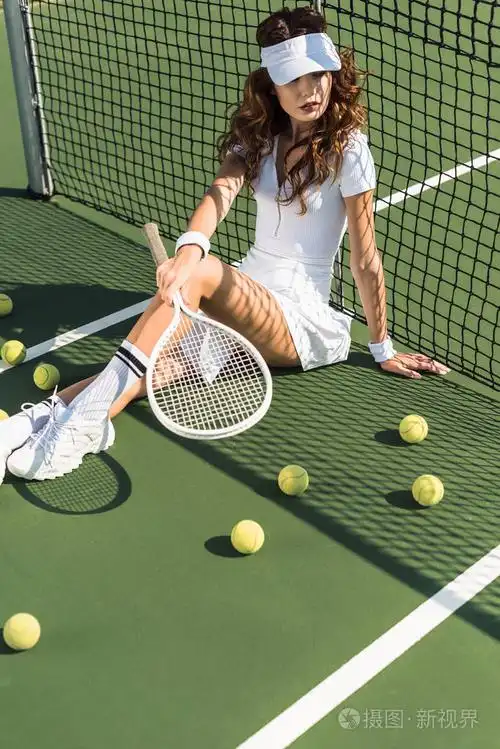 时髦网球运动员在白色运动服与网球球拍坐在网在网球场