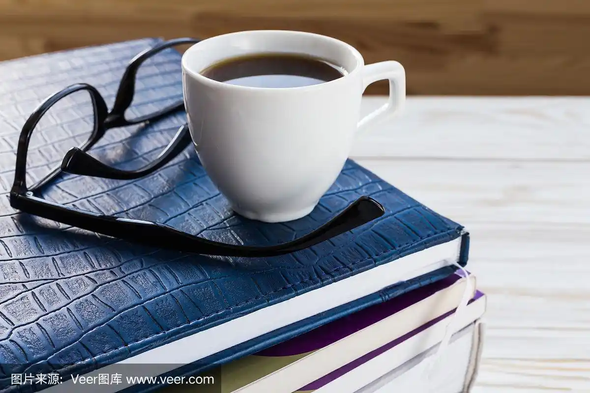 玻璃杯,一杯热咖啡和木桌上的书