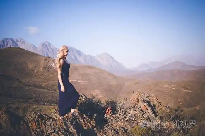 美丽的金发女模特站在山上欣赏风景