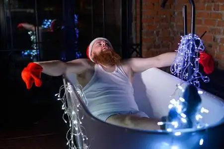 一个戴着圣诞老人帽,穿着内衣的红胡子男人手里拿着一个花环.照片