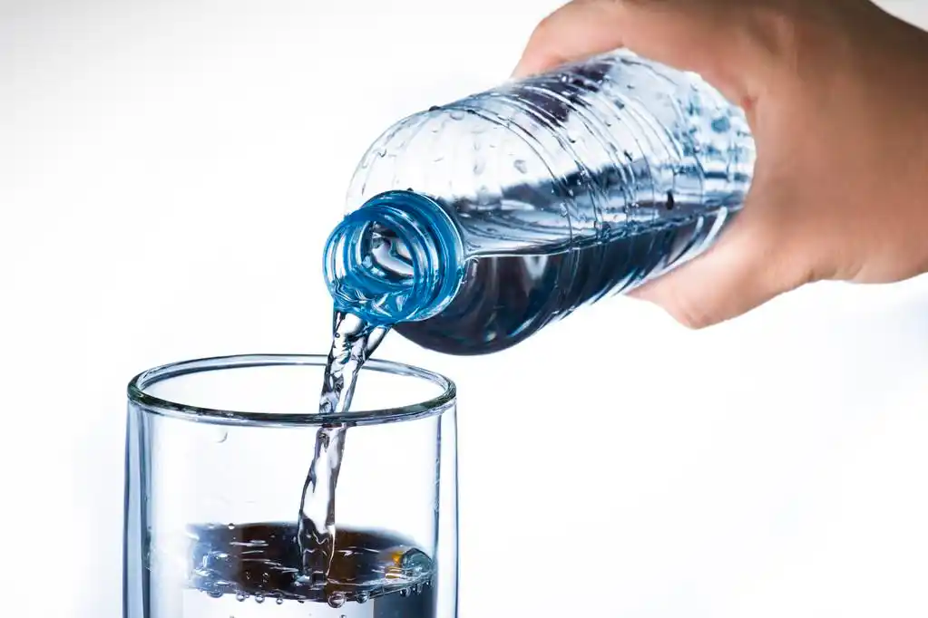 倒入玻璃杯的水,手拿着矿泉水瓶倒入玻璃