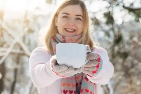 粉毛衣年轻的白种人迷人的金发女孩粉红色毛衣和针织围巾举行杯热茶在