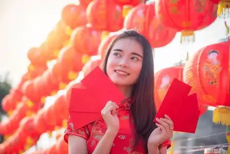 身着中国传统服装的美丽亚洲女孩在中国红灯笼前微笑着拿着红包钱照片