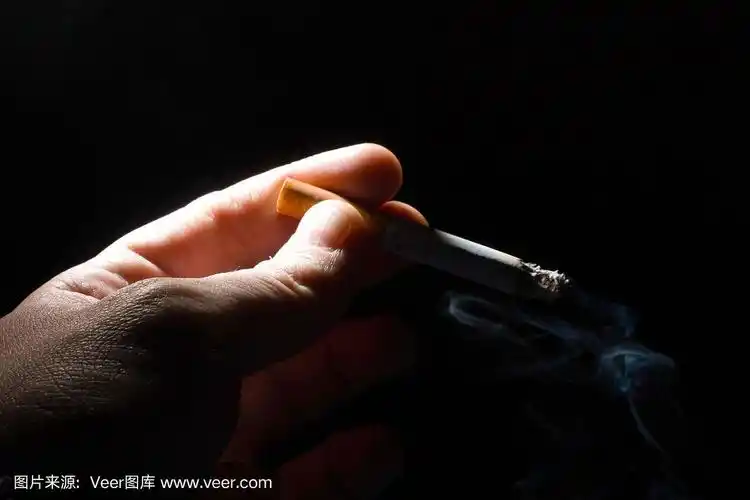 手握一根燃烧着的香烟在黑色背景的拷贝空间上冒烟.近距离