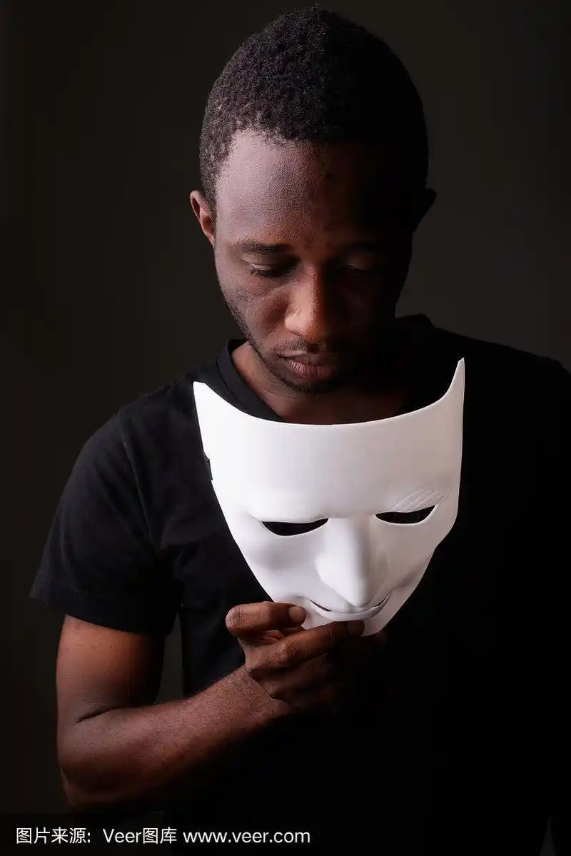摄影棚拍摄的年轻非洲黑人男子在黑暗的房间里拿着面具向下看