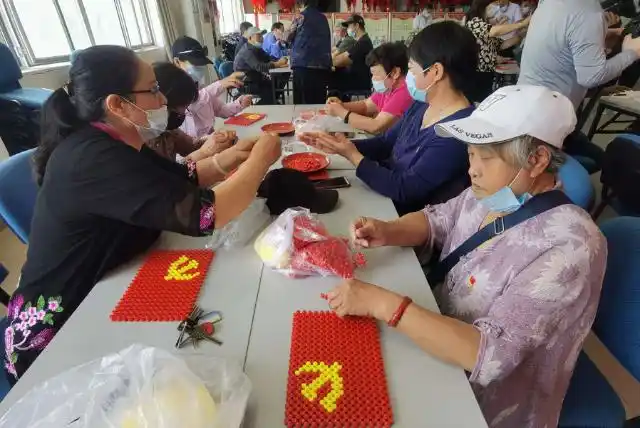 党员们通过用手工串珠编织党旗的方式传承党的红色基因,迎接建党100