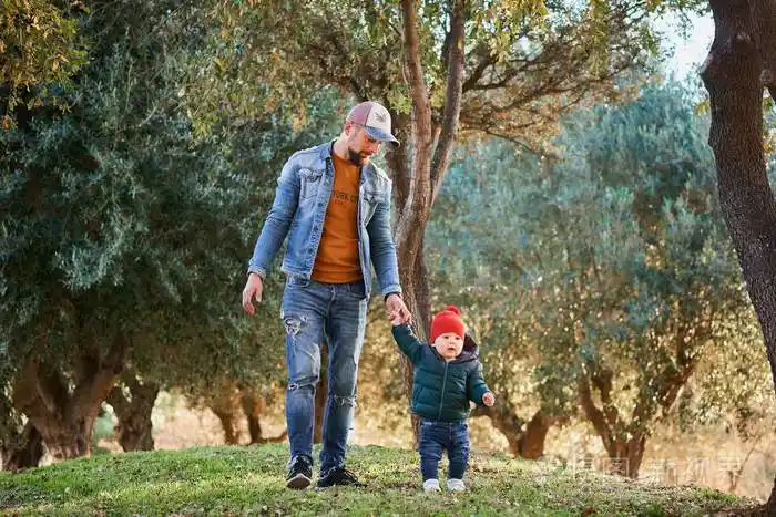 阳光明媚的一天可爱的小男孩和他的父亲一起在公园里散步一对父子带着