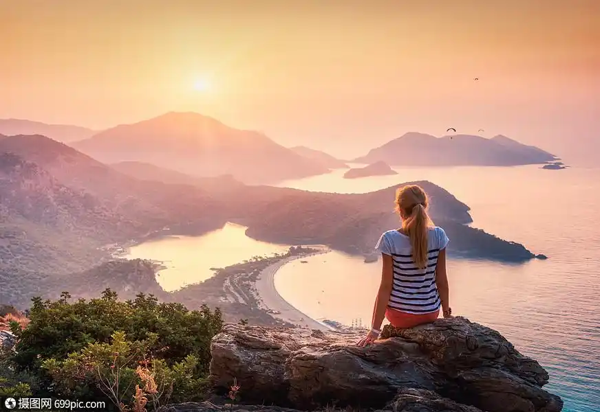 轻的女人坐岩石的顶端,看着海边轻的女人坐岩石的顶