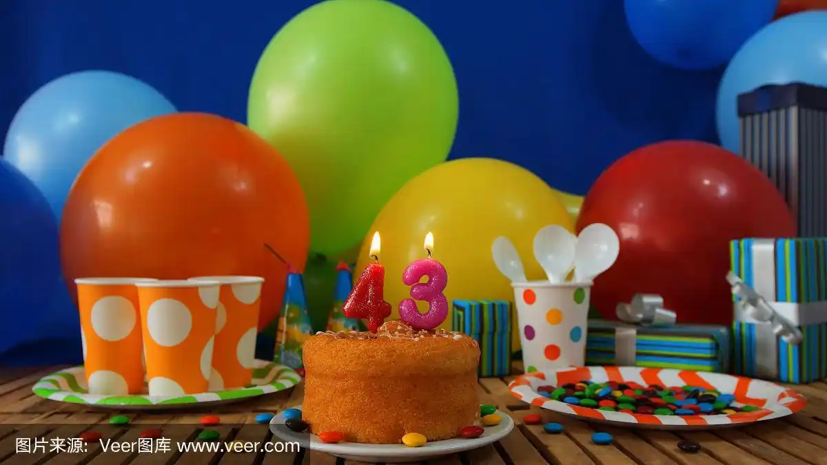 43岁生日蛋糕放在质朴的木桌上,背景是彩色的气球,礼物,塑料杯和塑料