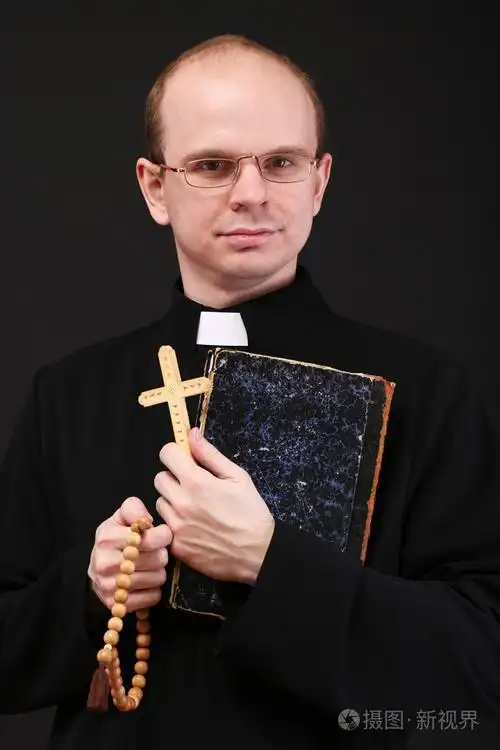 年轻牧师与木制十字架和圣经,孤立在黑色