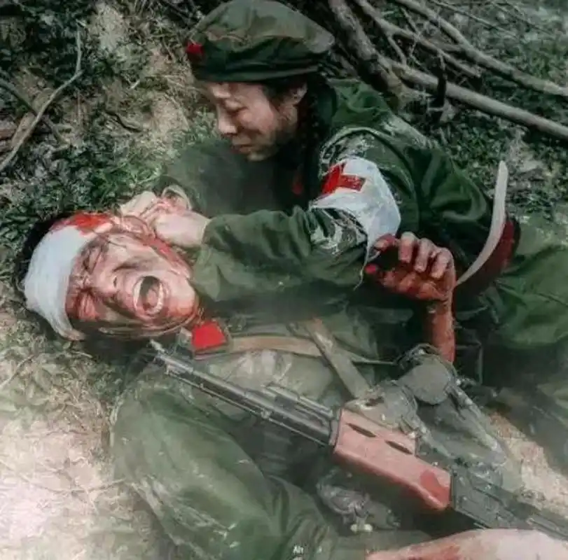 1979年老山战役中,一名年轻的战士躺在地上,一位护士正在给他包扎头部