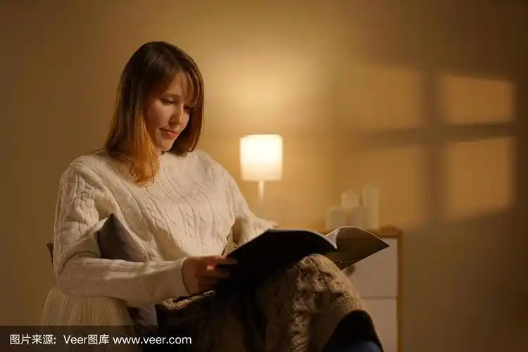 一个漂亮的女孩晚上坐在家里舒适的椅子上看书.