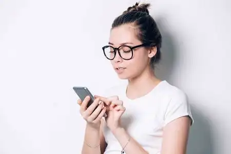 愉快的年轻红发女学生用逗人喜爱的微笑, 使用手机, 俏丽的女孩冲浪