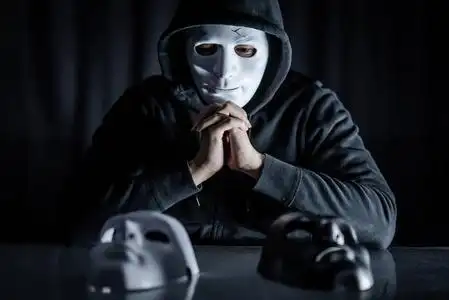 帽衫男戴着神秘面具,在桌子上选择黑色或白色面具. 匿名社交伪装.